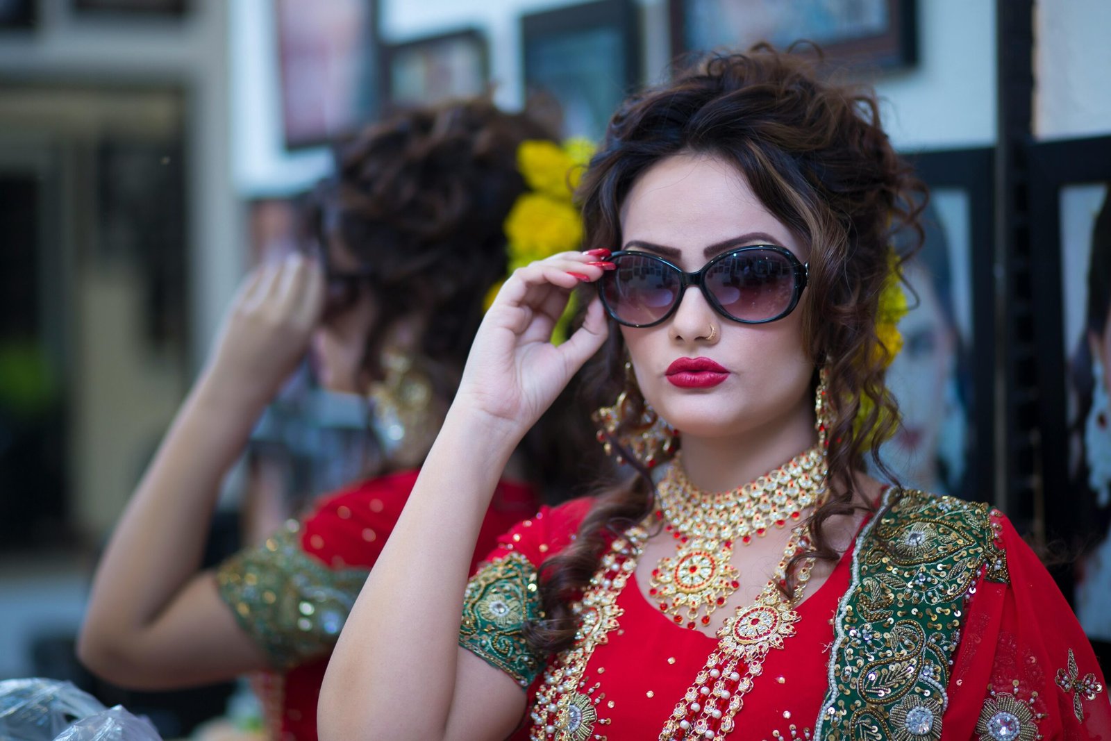 Home Beautiful South Asian bride in traditional red attire, adorned with jewelry and sunglasses, posing indoors.